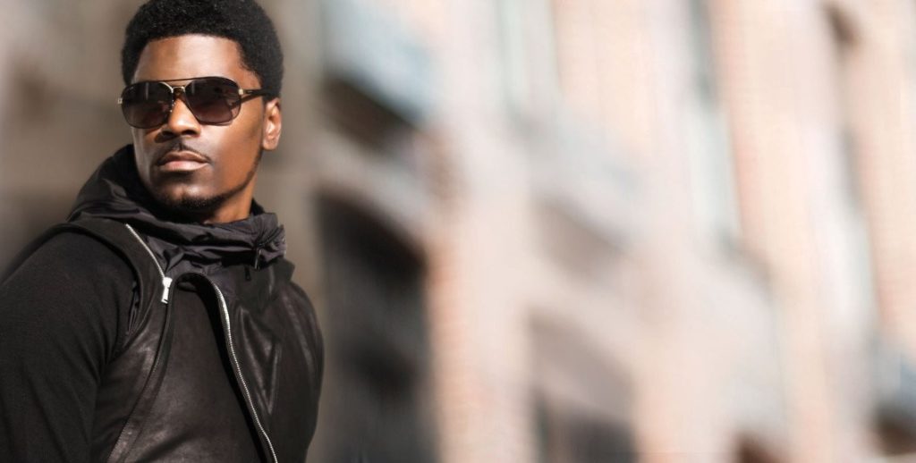 Glen Lewis wearing dark sunglasses looking into the distance, against an apartment building background