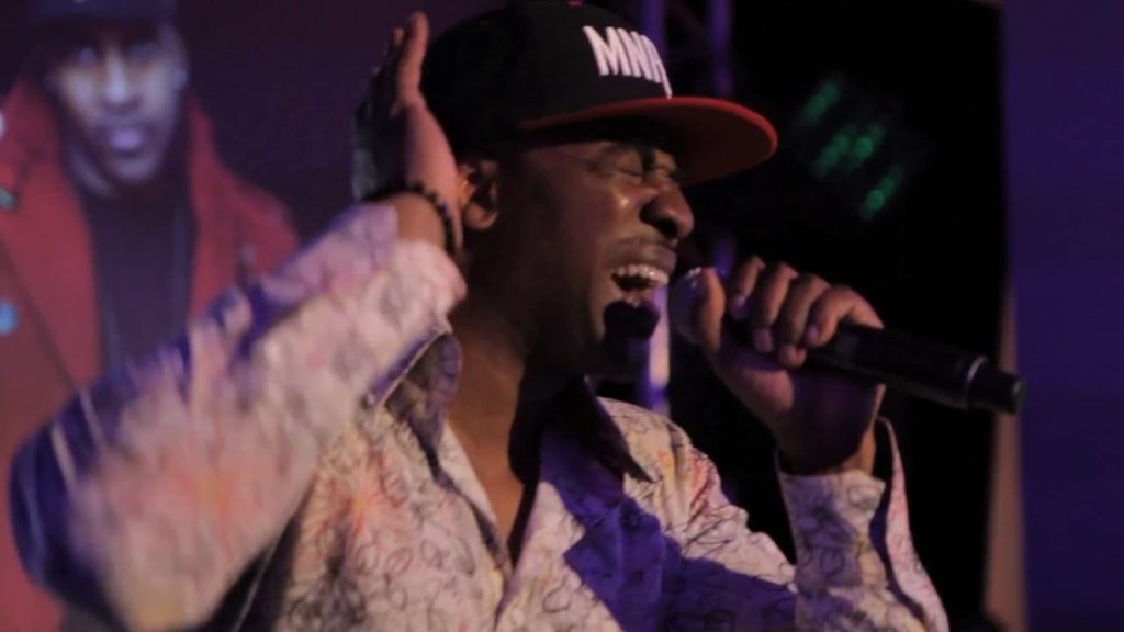 Maestro singing into a microphone wearing a red cap and blue shirt