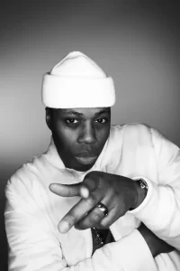 Kardinal Offishall posing with his hands for photo shoot, wearing a white hat and sweater.