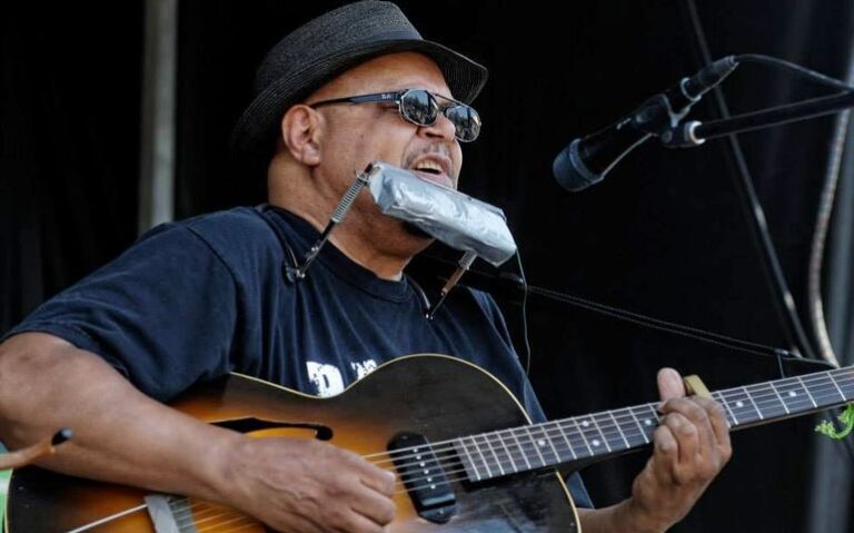 Harrison Kennedy singing into the microphone and playing his guitar during a performance.