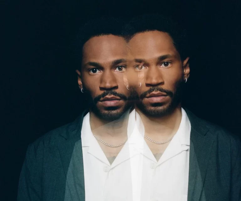 Kaytranada wearing a white shirt, standing confidently.