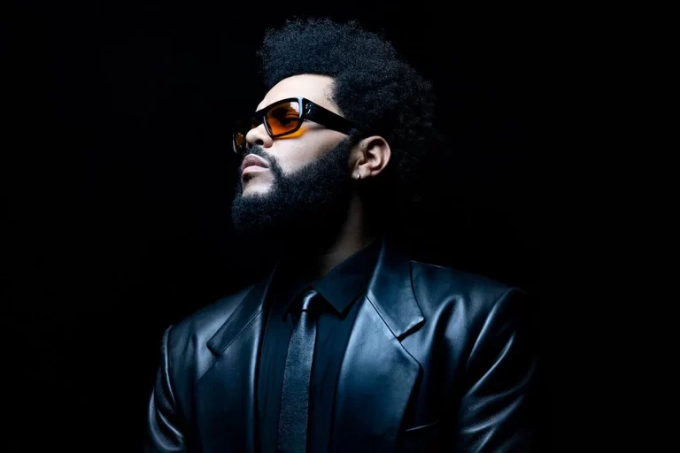 The Weeknd in a leather suit and sunglasses, posing confidently for a photo shoot.