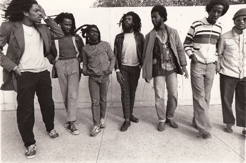 Black & white image of band members standing casually in front of a wall.