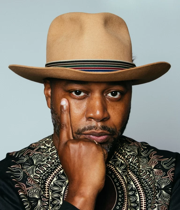 Dwayne Morgan posing in front of blue-ish background with finger rested on cheek