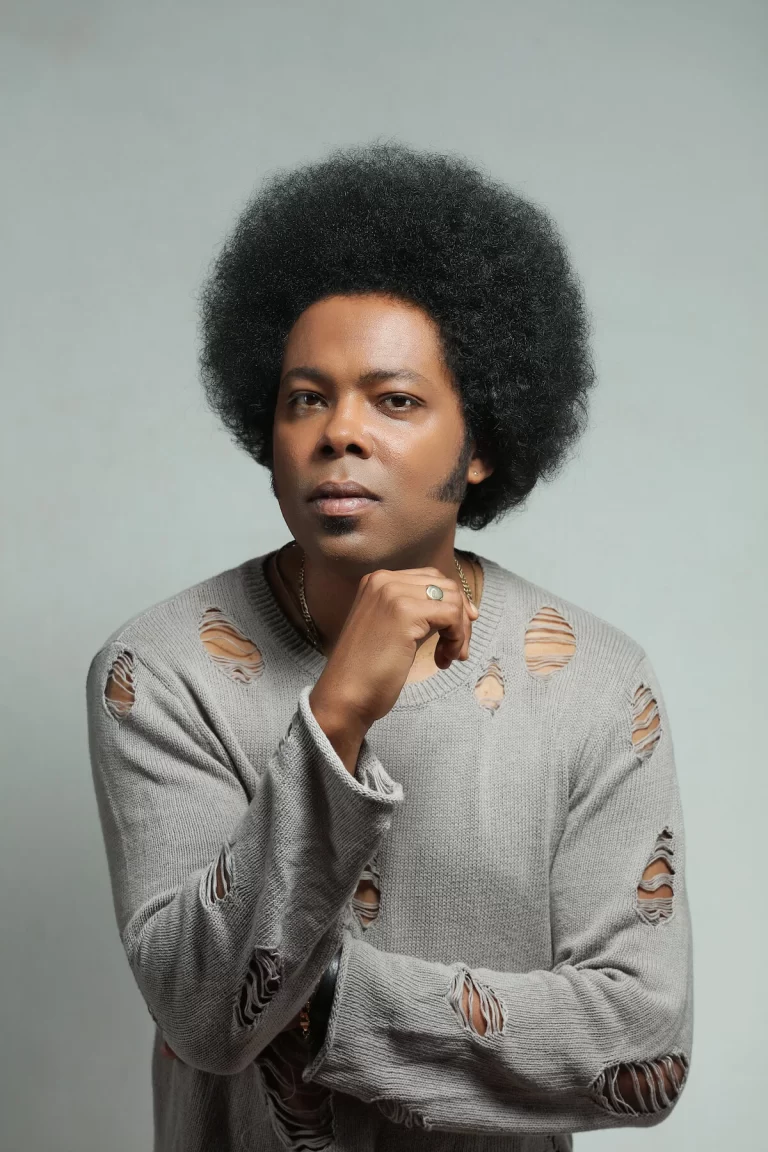 Alex Cuba posing in ripped sweater, hand under chin