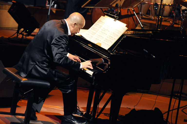 Hilario Duran playing piano on stage, wearing black tux