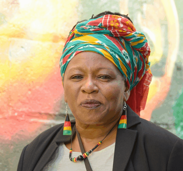 Carol Brown in front of Reggae Lane mural with colourful head scarf and Rasta coloured earrings
