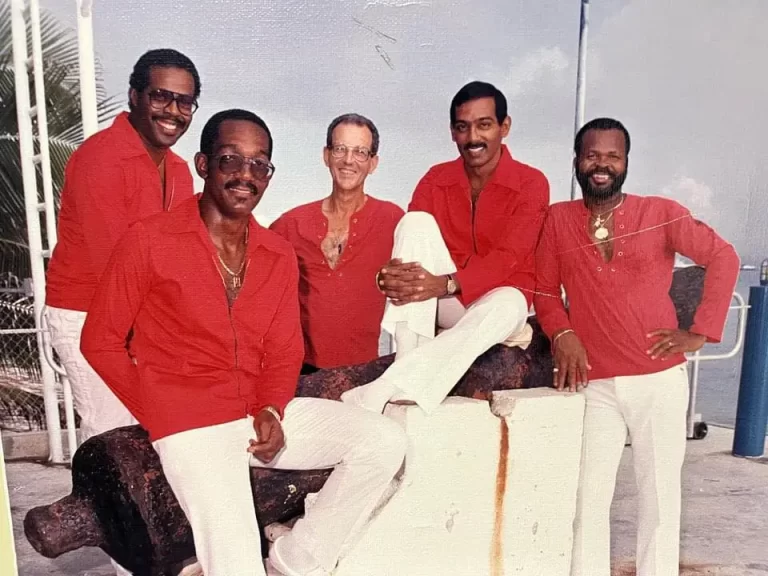 Tradewinds band posing by water, dressed in red shirts and white pants