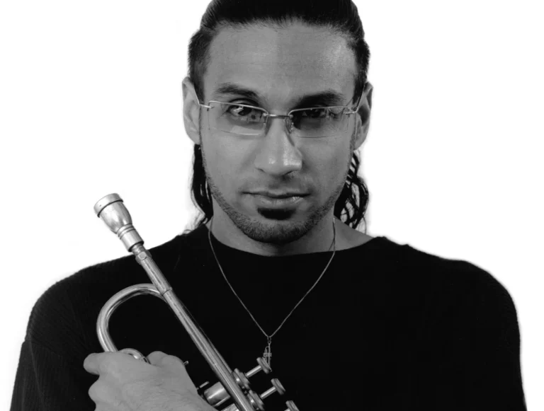 Black and white photo of Brownman holding trumpet to chest, wearing glasses