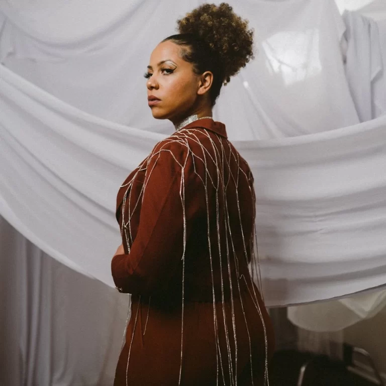 Joanna Majoko dressed in red and looking back at camera, white drapes in background