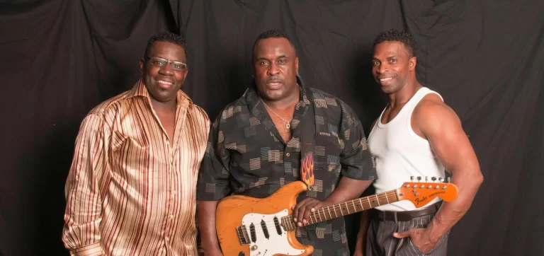 Carson Downey Band posing in front of black backdrop, with guitar