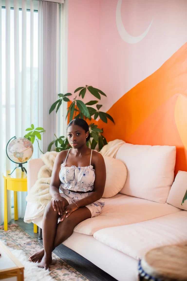 Sammy Jackson sitting on couch in colourful living room in front of plant, on white couch