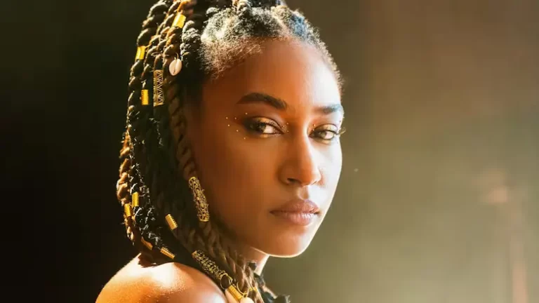 Close-up of Dominique Fils-Aimé looking over shoulder into camera, adorned with gold