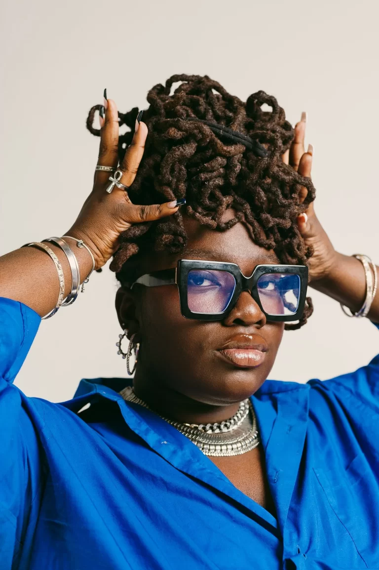 Shahaddah Jack with hands on hair, looking into camera, wearing blue shirt and glasses