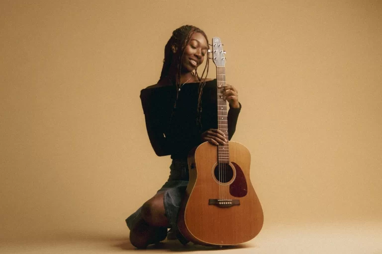 Bukola sitting and posing with a guitar.