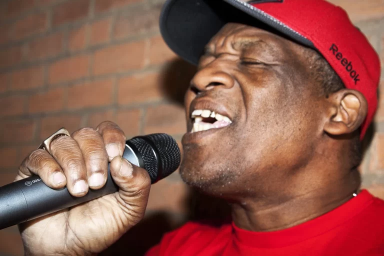 Close-up of Jah Cutta singing into microphone, wearing red