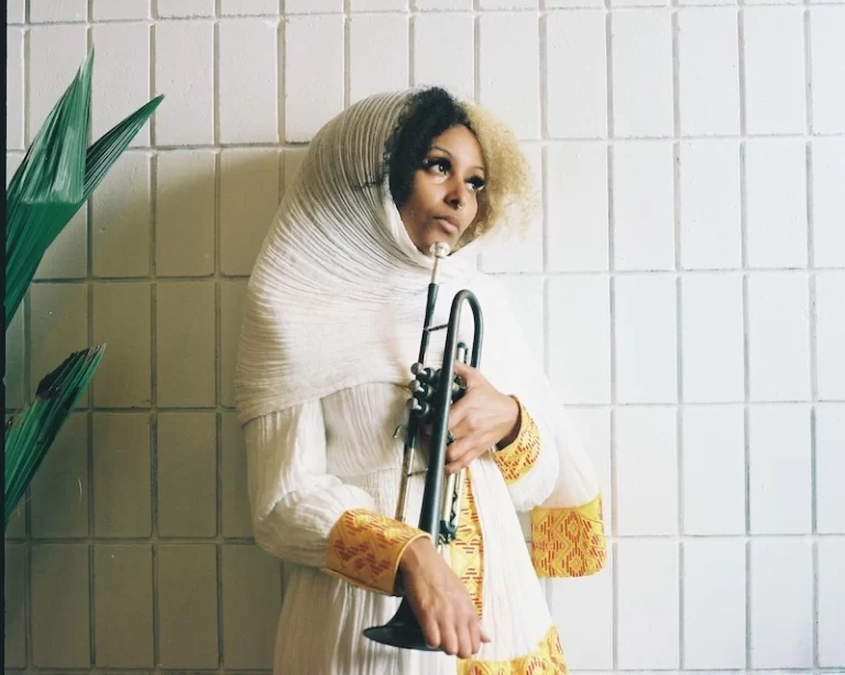Feven holding a trumpet in white Ethiopian attire.