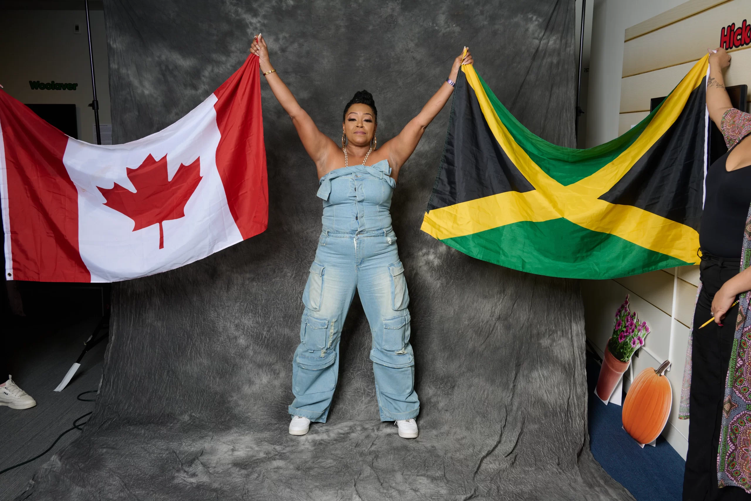 Interior, wide shot of Michie Mee with arms raised above her head holding the Canadian flag in her right hand, and Jamaican flag in the other.